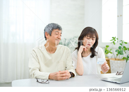 リビングでパソコンとカードを見る60代の夫婦 リビングでパソコンとカードを見る60代の夫婦 136566912