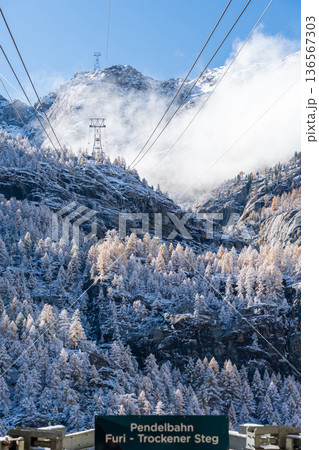 霧のかかった雪山を背景にしたフーリからトロッケナー・シュテックへのロープウェイ。ツェルマット、ヴァレ 136567303