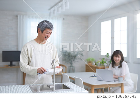 キッチンで皿洗いをする60代男性と会話をする女性 136567345