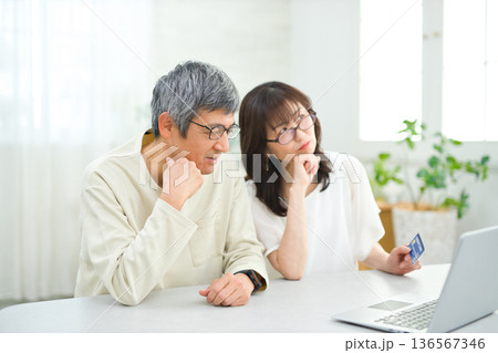 リビングでパソコンとカードを見る60代の夫婦 136567346