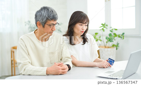 リビングでパソコンとカードを見る60代の夫婦 136567347