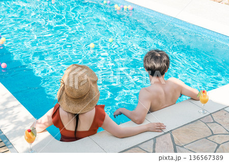 旅行先のリゾートホテルのプールサイドで遊ぶ水着姿のカップル,夫婦の後ろ姿 旅行先のリゾートホテルのプールサイドで遊ぶ水着姿のカップル,夫婦の後ろ姿 136567389