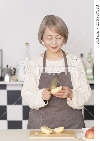 キッチンでりんごの皮をむくシニア女性 136567573