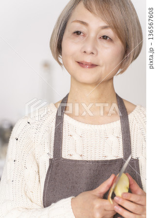 キッチンでりんごの皮をむくシニア女性 136567608