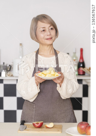 キッチンでりんごの皮をむくシニア女性 136567617