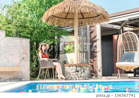 アジア人リゾートのプールサイドでデッキチェアに座る水着姿の若いアジア人女性 136567741