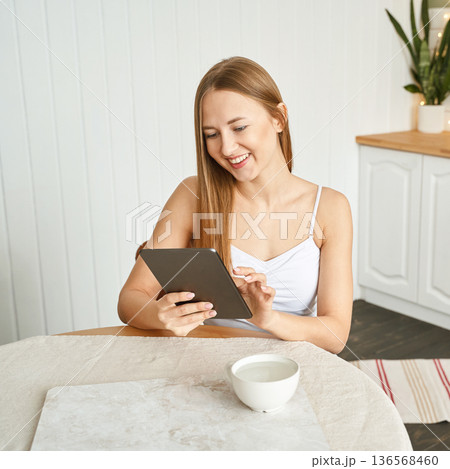 Young caucasian female using tablet in bright kitchen setting Young caucasian female using tablet in bright kitchen setting 136568460