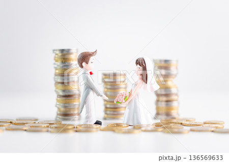 Bride and groom figurines holding bouquet stand among scattered coins with stacked money in background on clean white studio set, symbolizing smart wedding budgeting savings. budgeting savings Bride and groom figurines holding bouquet stand among scattered coins with stacked money in background on clean white studio set, symbolizing smart wedding budgeting savings. budgeting savings 136569633
