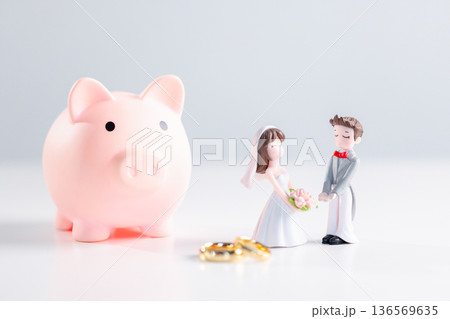 Pink piggy bank beside bride and groom figurines with bouquet and gold rings on clean white background, illustrating smart money planning for marriage, wedding savings and budgeting. money planning 136569635