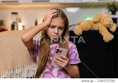 Teenager girl sees defeat alert on smartphone disappointed reaction sigh frown looks down quiet mood 136572793