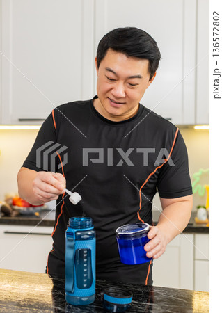 Asian man mixing supplement powder in shaker bottle shaking electrolyte recovery drink at home gym 136572802