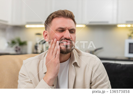 Young man with strong tooth pain covers cheek grimaces massages temple tries to ease sharp ache care 136573858