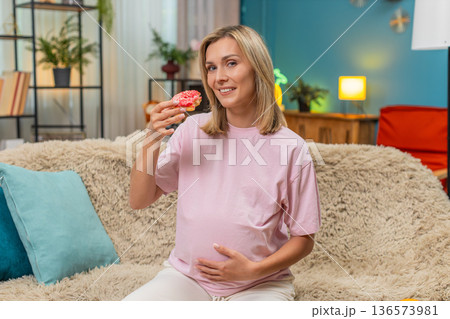 Pregnant woman eating donut with appetite smiling enjoying sugary treat during pregnancy craving joy Pregnant woman eating donut with appetite smiling enjoying sugary treat during pregnancy craving joy 136573981