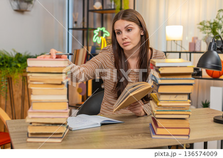 Young woman with stack of books writes notes from book looks very drained yet keeps focus on study Young woman with stack of books writes notes from book looks very drained yet keeps focus on study 136574009