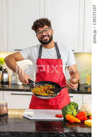 Arabian young adult man tasting vegetables from pan in kitchen cooking healthy dinner recipe at home Arabian young adult man tasting vegetables from pan in kitchen cooking healthy dinner recipe at home 136575107