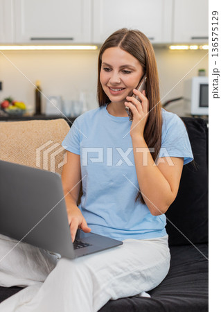 Young woman works on laptop and talks on smartphone multitasks with focus handles tasks and client Young woman works on laptop and talks on smartphone multitasks with focus handles tasks and client 136575129