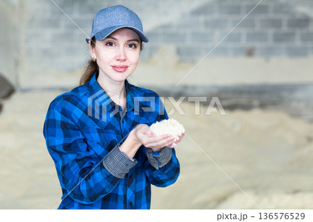 Woman checks the quality of cornmeal in an animal feed warehouse 136576529