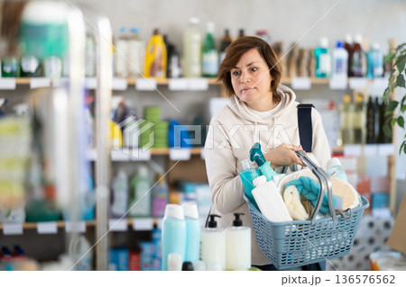 Woman with filled basket wanders around store, looking at display cases and inspects assortment 136576562