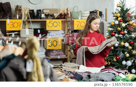 Teen girl is busy looking at clothes items in store, she choose trousers Teen girl is busy looking at clothes items in store, she choose trousers 136576590