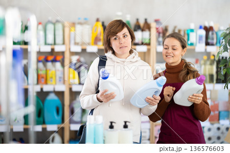 Young saleswoman offering detergent to female customer Young saleswoman offering detergent to female customer 136576603
