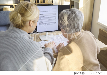 Closeup Daughter Helping Grandmother Pay Utility Invoices Online at Home Computer 136577255
