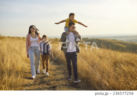 Cheerful family enjoying golden hour walk, kids riding shoulders at sunset 136577256