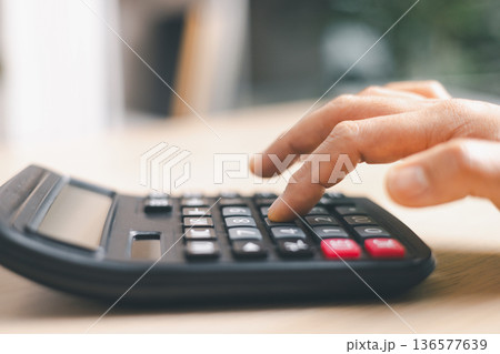 Close-up of a hand pressing calculator keys for budgeting, accounting and financial analysis. Business expense planning, tax calculation, office desk background, copy space for paperwork. Close-up of a hand pressing calculator keys for budgeting, accounting and financial analysis. Business expense planning, tax calculation, office desk background, copy space for paperwork. 136577639
