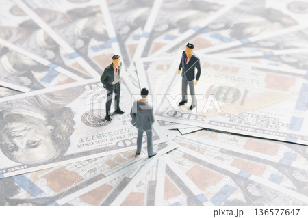 Miniature businessmen meeting on spread US dollar banknotes, symbolizing investment, negotiation and financial strategy. Business finance concept with cash background and copy space. Miniature businessmen meeting on spread US dollar banknotes, symbolizing investment, negotiation and financial strategy. Business finance concept with cash background and copy space. 136577647