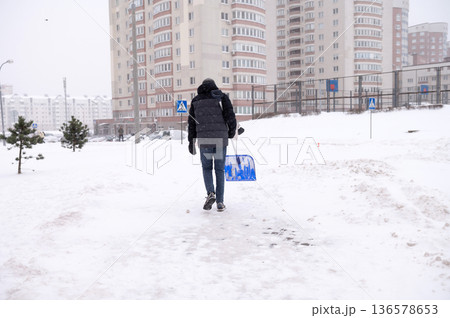 Male in winter attire shoveling snow in urban residential area 136578653