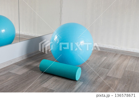Blue exercise ball and foam roller on wooden floor near a mirror Blue exercise ball and foam roller on wooden floor near a mirror 136578671