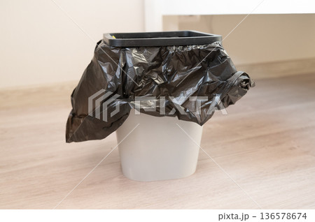 Empty trash bin with black plastic liner on wooden floor 136578674