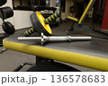 Gym equipment on bench with ab roller and dumbbell bar in fitness center 136578683