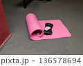 Pink yoga mat, eye mask, and pillow on gray floor in gym setting 136578694