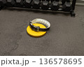 Weightlifting belt on yellow plate in gym with black dumbbells on rubber flooring 136578695