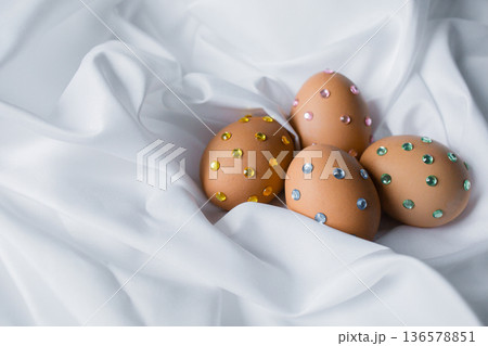 Easter eggs decorated with colorful crystal rhinestones on white silky fabric Easter eggs decorated with colorful crystal rhinestones on white silky fabric 136578851