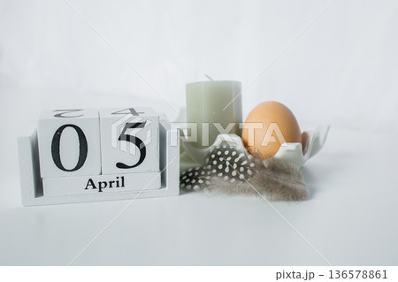 Christian Catholic Easter 2026 date on a wooden calendar with Easter egg, chicken feather and decorative candle on white background close up 136578861