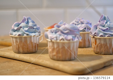 Person decorating cupcakes. Baker piping swirl of a creamy blue purple frosting onto a freshly baked cupcake. Decorated cakes with colorful sprinkles. Sweet Dessert Preparation. Pastry small business Person decorating cupcakes. Baker piping swirl of a creamy blue purple frosting onto a freshly baked cupcake. Decorated cakes with colorful sprinkles. Sweet Dessert Preparation. Pastry small business 136579114