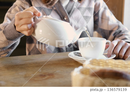 Young teen girl enjoying a break, drinking tea from a white porcelain cup in a modern cafe setting. Teapot is on a table. Teenager female drinking hot tea indoors. Relaxing moment. Hot beverage Young teen girl enjoying a break, drinking tea from a white porcelain cup in a modern cafe setting. Teapot is on a table. Teenager female drinking hot tea indoors. Relaxing moment. Hot beverage 136579139