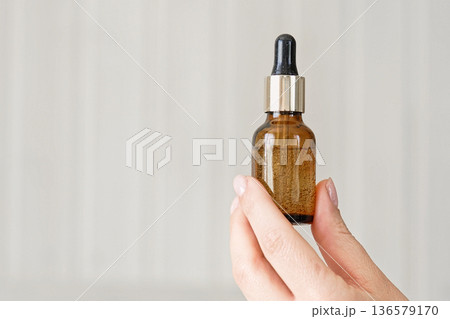 Female hands showing natural oil cosmetics on a Beige Background. Dropper amber brown glass Bottle with pipette. Spa Beauty products Isolate on Neutral Backdrop. Skincare recommend, makeup advertising 136579170