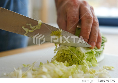 Handsome bearded man is preparing green fresh vegan salad in the kitchen at home. Male cutting vegetables, lettuce with knife on wooden chopping board, cooking vegetarian meal. Tasty healthy diet food Handsome bearded man is preparing green fresh vegan salad in the kitchen at home. Male cutting vegetables, lettuce with knife on wooden chopping board, cooking vegetarian meal. Tasty healthy diet food 136579175