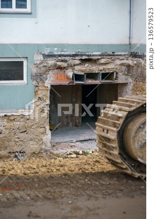 Heavy machinery dismantling damaged facade of residential building during renovation works, construction site with debris and exposed structure. 136579523