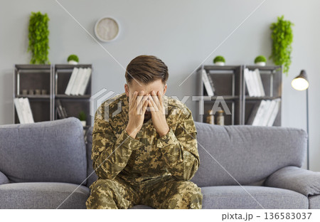 Male soldier in uniform sitting on sofa alone facing post-traumatic stress disorder 136583037