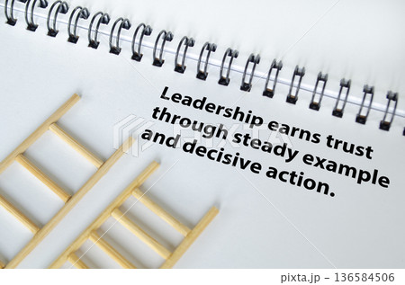 LEADERSHIP earns trust concept text on white notepad with ladders background. 136584506