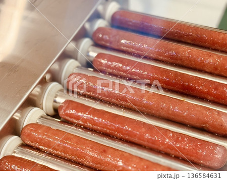 Long delicious hot dogs are sizzling on a roller grill in supermarket indoor, making them the perfect choice for outdoor gatherings and events. Close-up Long delicious hot dogs are sizzling on a roller grill in supermarket indoor, making them the perfect choice for outdoor gatherings and events. Close-up 136584631