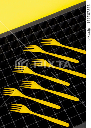 Still life with yellow plastic forks on a surface with cells. Still life with yellow plastic forks on a surface with cells. 136587828