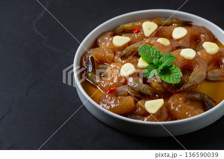 Korean style soy marinated shrimp served with garlic slices, chili, and fresh herbs in a white bowl on dark background. Popular Korean seafood dish known as saeu jang, premium raw shrimp, Korean style soy marinated shrimp served with garlic slices, chili, and fresh herbs in a white bowl on dark background. Popular Korean seafood dish known as saeu jang, premium raw shrimp, 136590039