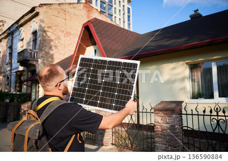 Man holding photovoltaic solar panel in front of historical building. Concept of integration of sustainable renewable energy sources into architecture. 136590884