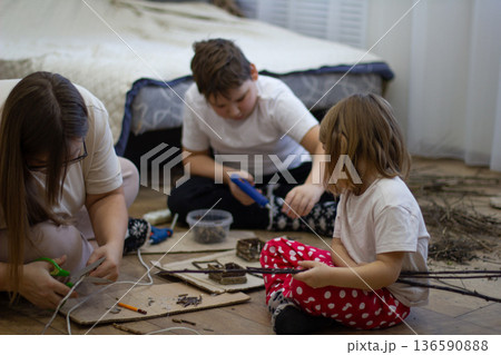 Mother and children create crafts together on the floor using tree branches, cardboard, and various natural materials. Creating crafts together fosters creativity and strengthens relationships. Mother and children create crafts together on the floor using tree branches, cardboard, and various natural materials. Creating crafts together fosters creativity and strengthens relationships. 136590888