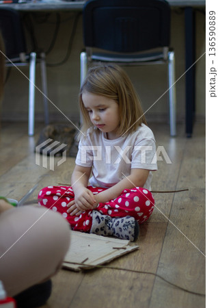 Vertical. A girl sits on a wooden floor, intently creating crafts from natural materials and cardboard during an art workshop. The child develops creativity through learning. Vertical. A girl sits on a wooden floor, intently creating crafts from natural materials and cardboard during an art workshop. The child develops creativity through learning. 136590889