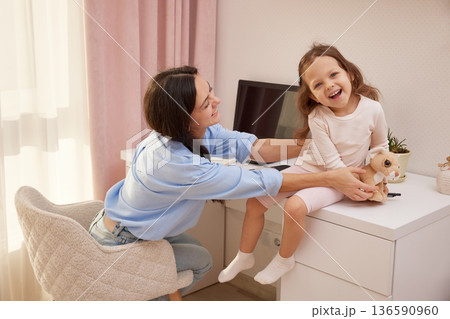 Mother and daughter smiling while interacting in a home office environment Mother and daughter smiling while interacting in a home office environment 136590960